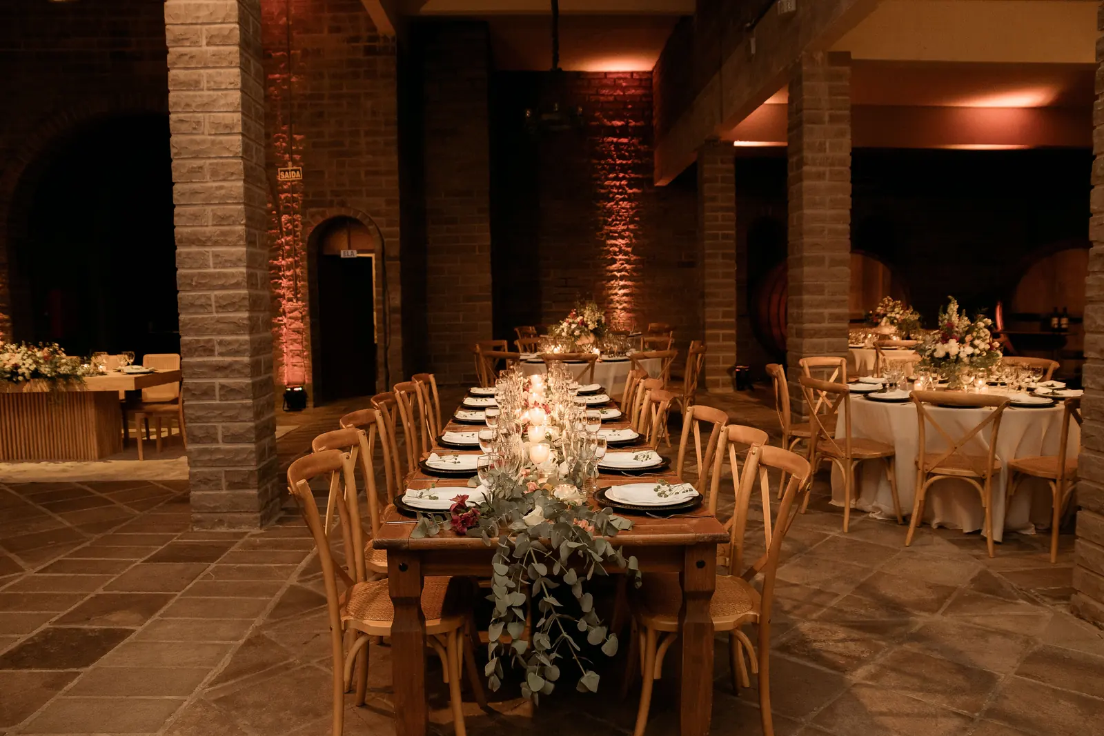 A long wooden table laid with plates and glasses beneath brick pillars in a warmly lit hall