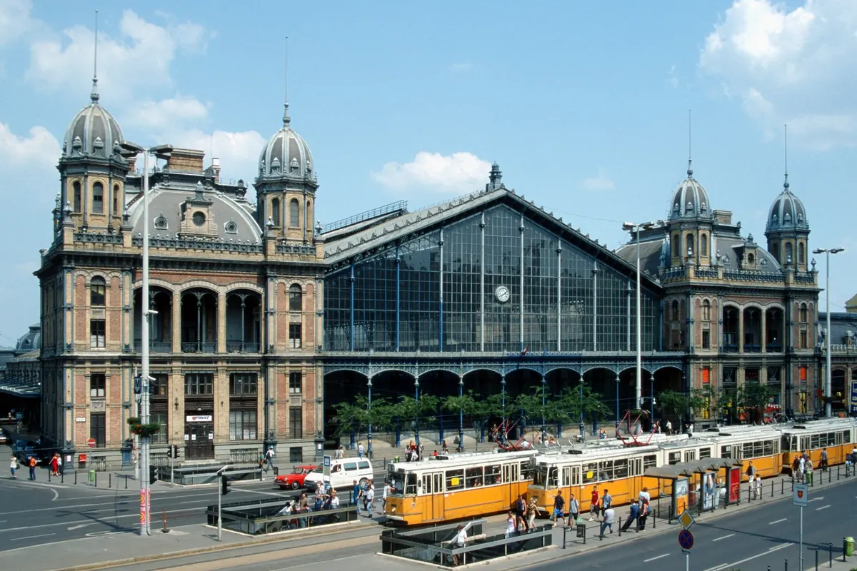 Nyugati station's ornate stone front and glass-and-iron hall, with yellow trams in the foreground