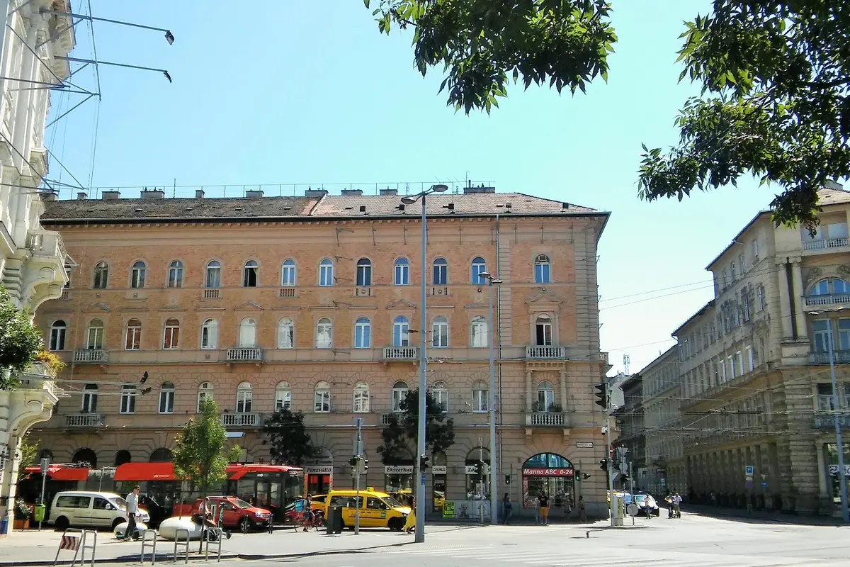 A pale pink apartment building with arched ground-floor windows on a tree-lined corner of Podmaniczky utca in Budapest
