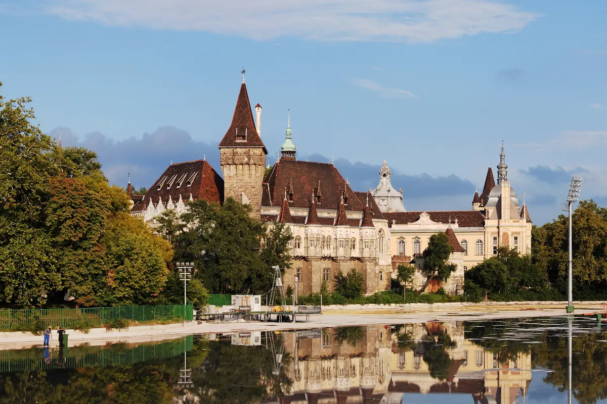 Vajdahunyad Castle in Budapest's City Park, a turreted brick-and-stone castle reflected in the lake under a blue sky